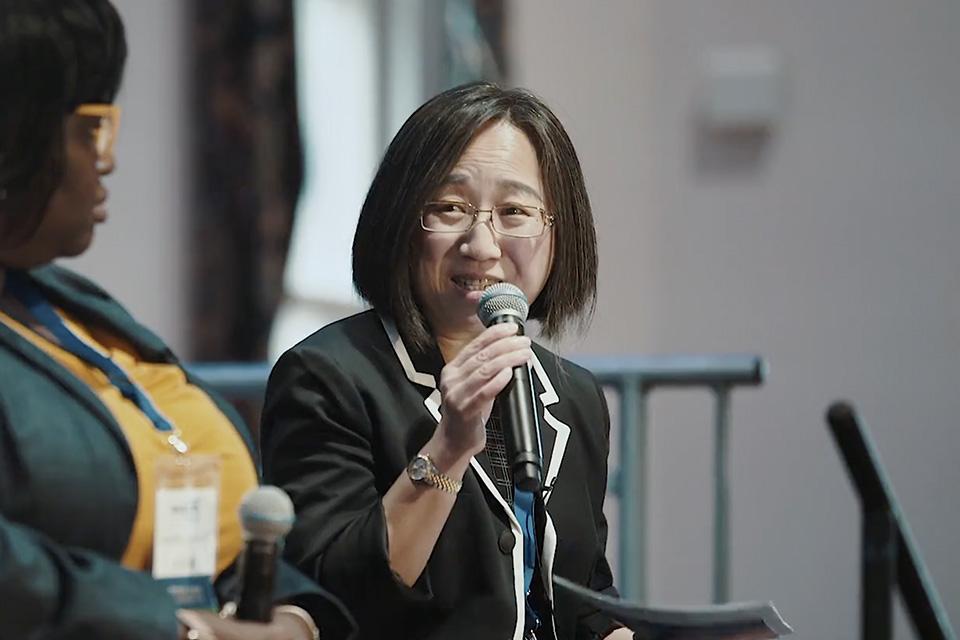 A woman sits and smiles while holding a microphone.